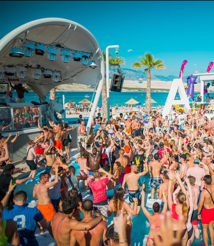 Pool party at Zrce Spring Break on Zrće Beach with palms, the sea and the Velebit mountains behind